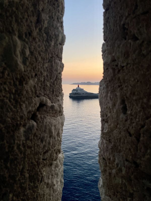 Le phare de la Madonetta à Bonifacio au coucher du soleil, vu à travers une meurtrière des remparts