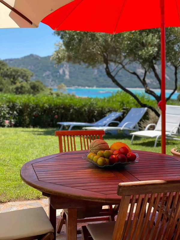 La table en bois de la terrasse sous le parasol, face au jardin et à la baie de Santa Giulia
